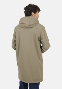 Manteau beige imperméable avec capuche, présentant un design mi-long et une texture lisse, des coutures visibles et une silhouette simple.