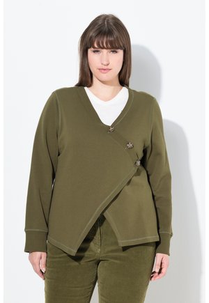 Cardigan avvolgente verde oliva in un tessuto morbido, con scollatura a V, bordi cuciti e bottoni distintivi come dettagli, abbinato a pantaloni coordinati.