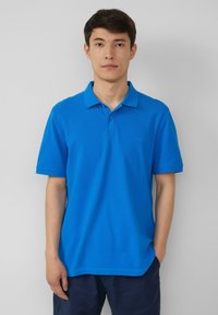 Blauwe katoenen polo met een kraag, korte mouwen en een subtiel logo op de linkerborst. Gladde textuur en een ontspannen pasvorm.