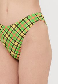 Hög midjebikiniunderdel i ett rutigt mönster i grönt, gult och orange. Tillverkad av stretchigt tyg med en mjuk textur och sömlösa kanter.