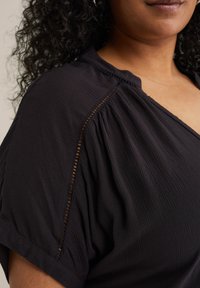 Čierny krátky rukávový top vyrobený z ľahkej textúrovanej látky, s V-čkovým výstrihom a jemnými vykrojeniami pozdĺž ramenných švov.