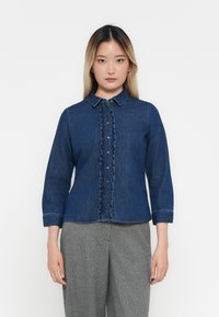 Denim särg volangidega esipaneeliga, tume sinine värv, nööpidega kinnitamine ja levinu krae. Pikad varrukad, mis lõpevad mansettidega.