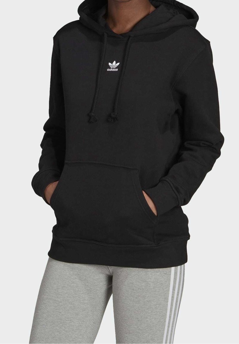 Svart hoodie med dragsko och känguruficka, med en vit Adidas-logotyp på bröstet. Bärs med grå leggings.