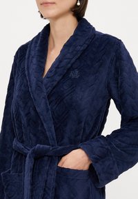 Námornícky modrý fleece župan s textúrovaným vzorom, skrytým dizajnom a viazaným pásom; má vyšívané logo "RL" na golieri.