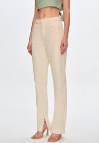Pantalones de pierna ancha de color beige claro, elaborados con una tela texturizada, que presentan un cierre de botón en la parte delantera y acentos de abertura lateral en el dobladillo.