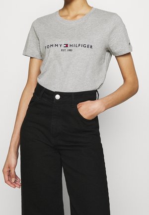 Grijs katoenen T-shirt met korte mouwen, met de tekst "TOMMY HILFIGER EST. 1985" in marineblauw en rood over de borst. Zwarte broek met hoge taille.