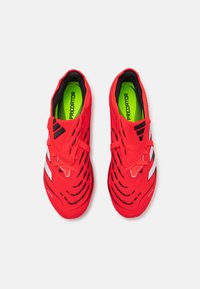 Red athletic shoes featuring a textured upper, streamlined design, and white accents. The interior has a bright green insole with branding.