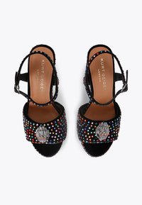 Czarne zamszowe sandały z wielokolorowymi cyrkoniami, z dekoracyjnym metalowym akcentem i paskiem na kostkę. Płaska podeszwa i otwarty przód.