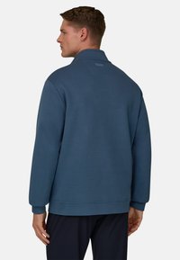 Sudadera azul oscuro de corte relajado, con cuello y puños acanalados. Presenta un branding minimalista en la parte trasera. Textura lisa.