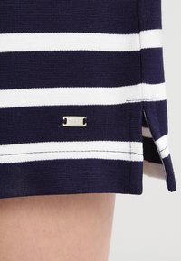 Fondo de prenda a rayas horizontales en azul marino y blanco con abertura lateral y pequeña etiqueta de marca metálica rectangular adjunta.