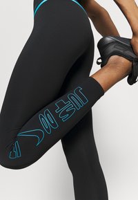 Mustat legginsit sinisillä yksityiskohdilla; sisältää tekstin "JUST DO IT" paksulla fontilla, valmistettu joustavasta kankaasta mukavuutta ja liikkuvuutta varten.