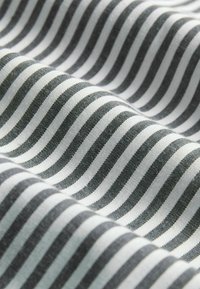 Nahaufnahme eines weichen Stoffs mit gleichmäßig verteilten schwarzen und weißen vertikalen Streifen, die sanfte Wellen bilden.