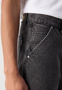 Svarta denimjeans med en lätt blekning, med en femficksdesign, metallnitar och en texturerad yta. Midjan har en varumärkesetikett.
