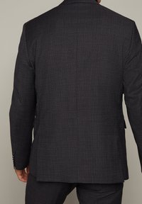 Mörk rutigt kostymjacka med en subtil mönstring, notch-lapel, strukturerade axlar och knäppta manschetter, tillverkad av texturerat tyg.