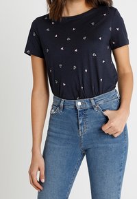 Námořnické tričko s krátkým rukávem, zdobené posetými růžovými srdíčky a diamantovými tvary. V páru s vysokými modrými džíny.