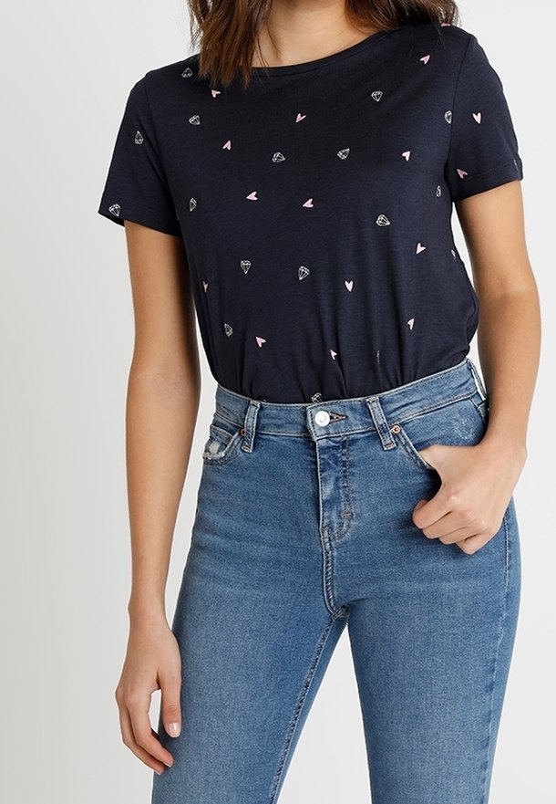 Námořnické tričko s krátkým rukávem, zdobené posetými růžovými srdíčky a diamantovými tvary. V páru s vysokými modrými džíny.