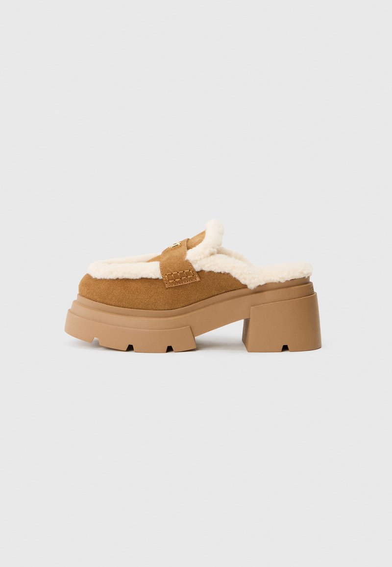 Scarpe slip-on in camoscio marrone con una morbida fodera color crema, suola piatta spessa e tacco a blocco. Presenta una fascia cucita sulla parte superiore.