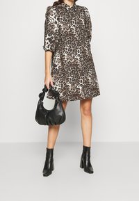 Leopardmönstrad klänning med polokrage, puffärmar och en A-linjeform. Bärs med en svart läderhandväska och klackade ankelstövlar.