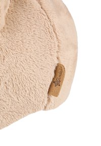 Beige plush ear muffs with a soft texture, featuring a brown leather tag with branding. Rounded shape providing full ear coverage.