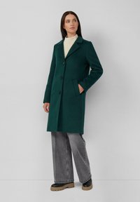 Teal wollen jas met een notch lapel, drie knopen, zijzakken en een rechte snit, gecombineerd met grijze wijde jeans en zwarte laarzen.
