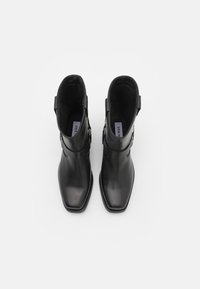Botas de cuero negro hasta el tobillo con puntera cuadrada, correas laterales y suelas planas. Interior forrado con tela para mayor comodidad. Diseño minimalista.