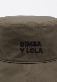 Oliwkowy kapelusz typu bucket wykonany z miękkiego materiału; na froncie haftowana czarna nazwa marki "BIMBA Y LOLA". Widoczne detale szwów.