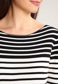 Haut à rayures noires et blanches avec un large décolleté, une texture côtelée et un tissu lisse. Présente des rayures horizontales de largeurs variées.