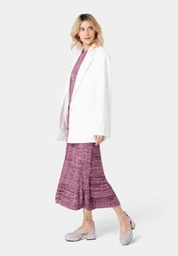 Blazer oversized blanc sur une robe texturée rose, dotée d'un design plissé. Associé à des chaussures à talons carrés en vernis rose clair.