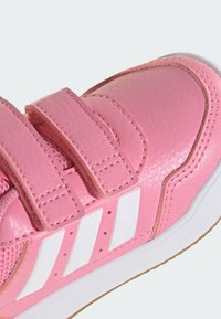 Ružová teniska so syntetickým zvrškom, dvoma nastaviteľnými suchými zipsami, bielym logom so tromi pruhmi a gumovou podrážkou s textúrovaným gripom.