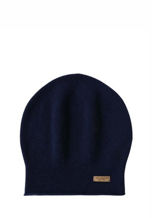 Cappello a cuffia di maglia blu navy con un'etichetta dorata brandizzata, abbinato a una sciarpa coordinata. Tessuto morbido, posato su un cappotto rosa chiaro e un maglione.