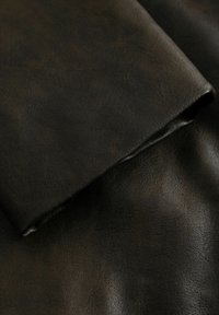 Fekete bőrszövet, puha, textúrált felülettel. Enyhén fényes vége van, és finom, változatos árnyalatok adnak mélységet.