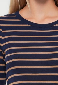Femme portant un t-shirt à rayures horizontales bleu marine et beige, mettant en valeur le décolleté et le haut de la poitrine.