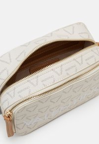 Borsa beige con zip e superficie texturizzata, con accenti dorati e motivo del logo "Valentino" ripetuto. Interno marrone. Design compatto.