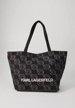 Czarna torba typu tote z powtarzającymi się białymi konturami twarzy Karla Lagerfelda oraz wyraźnym białym napisem "KARL LAGERFELD" na przodzie.