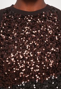 Top di paillettes con base in tessuto marrone, ricoperto di paillettes rotonde multicolori che riflettono la luce in tonalità di rosa dorato e marrone scuro.