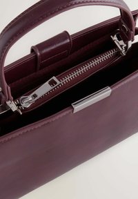Sac à main en cuir bordeaux au design structuré, doté d'une fermeture éclair et de quincaillerie en argent, avec une texture lisse et élégante.