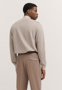 Beige strukturiertes Langarmhemd mit Kragen, kombiniert mit lockeren braunen Hosen mit Rückentaschen. Der Look ist casual und strukturiert.