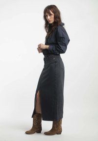 Jupe en denim foncé taille haute avec une fente sur le côté, associée à une chemise boutonnée sombre et des bottes de cowboy marron avec broderies florales.