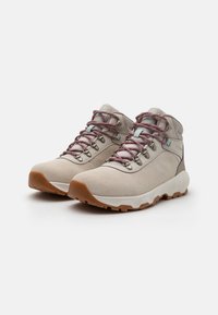 Lys beige fotturer med en teksturert semsket overdel, rosa og grå snørebånd, metalløyler og en kontrasterende gummisåle.