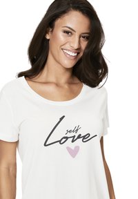 White cotton T-shirt with scoop neckline, featuring "self Love" printed in black and a light pink heart. Short sleeves and a relaxed fit.