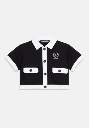 Crna skraćena košulja kratkih rukava s bijelim ovratnikom, prednjim zakopčavanjem na gumbe, manžetnama na rukavima, rubom, dva prednja džepa i malim izvezenim logotipom na prsima.