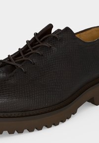 Gros plan d'une chaussure en cuir texturé marron foncé avec des lacets assortis et une semelle épaisse et robuste.
