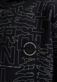 Sudadera negra con patrones gráficos y texto en blanco. Presenta un parche de logo circular con la palabra "PETROL" en el área izquierda del pecho.