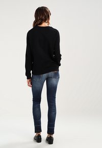 Un haut noir à manches longues avec un col rond, associé à un jean skinny bleu foncé présentant un léger délavage, et des chaussures noires.
