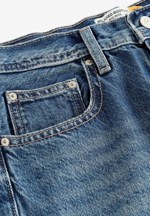 Kényelmes bootcut farmernadrág sötétkék színben. Közepes derékkal rendelkezik, rézvarrással, elülső zsebbel és fémből készült gombdíszítéssel.