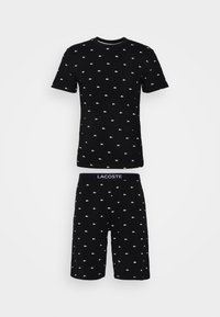 Sort bomulds pyjamasæt bestående af en kortærmet skjorte og shorts, begge med hvide Lacoste-logoer i et gentaget mønster.