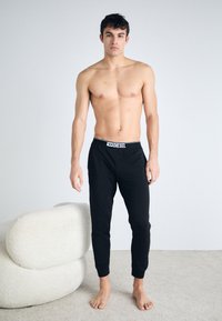 Pantalons de survêtement noir Diesel au design ajusté et à la taille élastique. Le matériau est doux et le pantalon se resserre au niveau des chevilles.