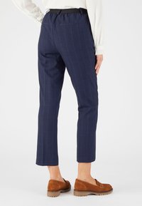 Marineblauwe broek met streepjes in een relaxte pasvorm, voorzien van een elastische tailleband en achterzakken, gecombineerd met bruine instapschoenen.