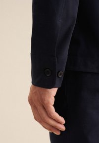 Navy katoenen blazer mouw met twee zwarte knopen aan de manchette, met een gladde textuur en een getailleerde pasvorm.