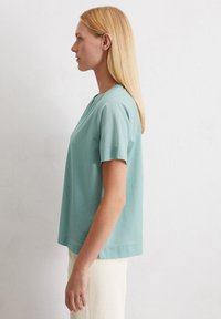 T-shirt a maniche corte in teal chiaro realizzato in un tessuto morbido, con scollatura rotonda e vestibilità comoda. Texture liscia con un design semplice.